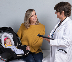 Woman with baby in carrier talking to healthcare provider.