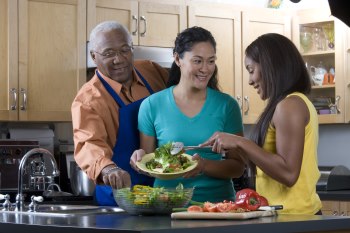 Family making a salad together. Mom is serving the daughter and the father is stealing a vegetable from the bowl